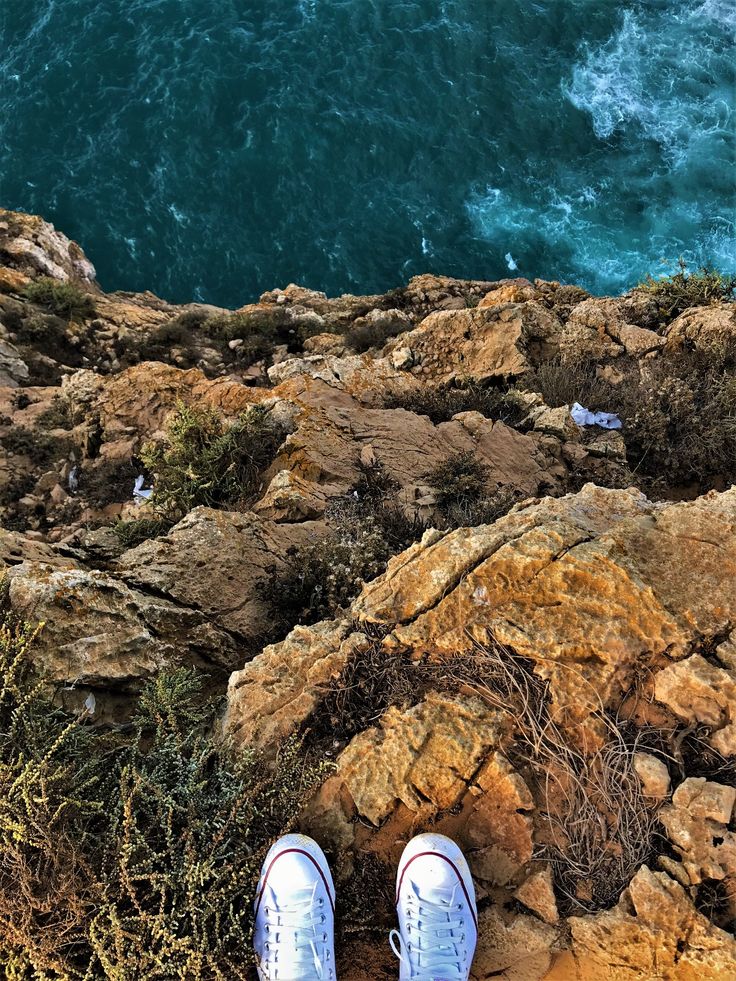 a pair of white shoes sitting on top of a rocky cliff next to the ocean