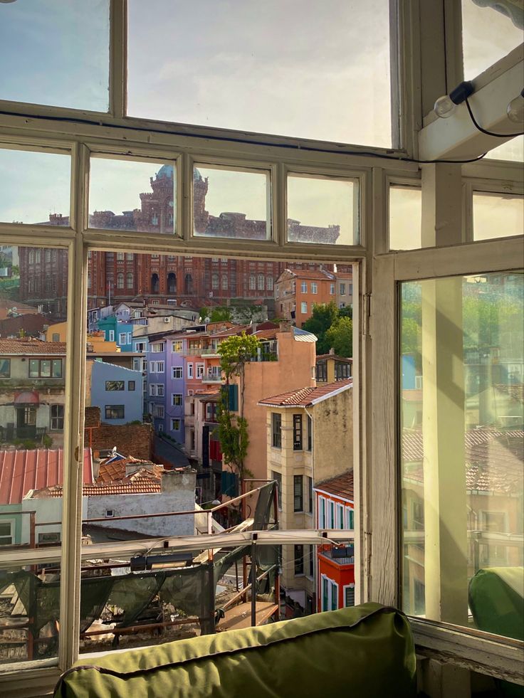 the view from an apartment window shows buildings and rooftops in the distance, with a green couch on the foreground