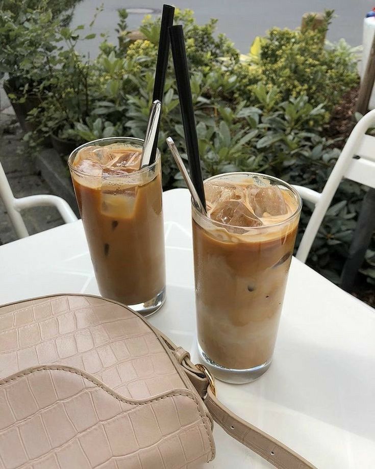 two iced coffees sitting on top of a white table next to a brown purse