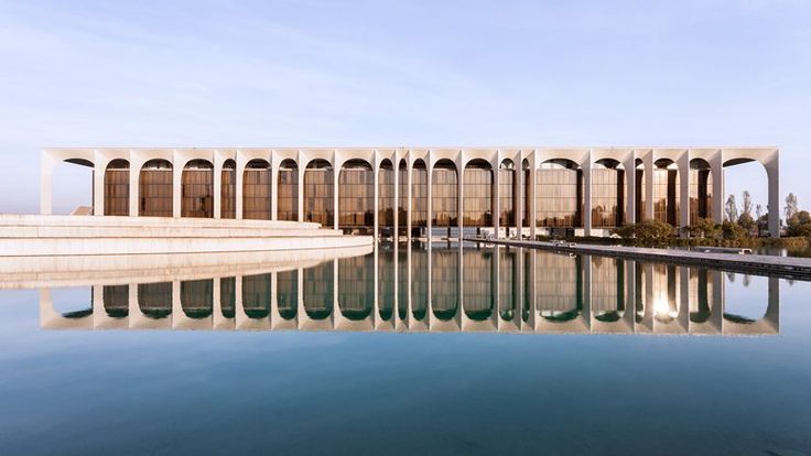 a large building sitting next to a pool in front of a blue sky and water