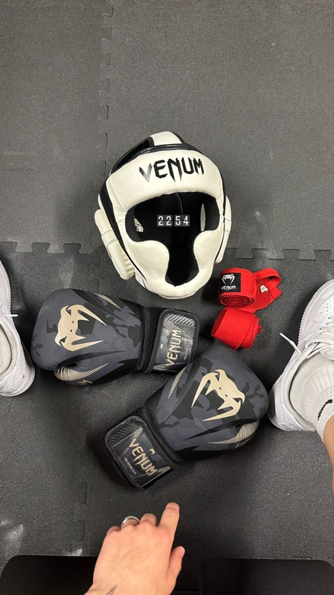 several pairs of boxing gloves sitting next to each other on the ground with one person's hand pointing at them