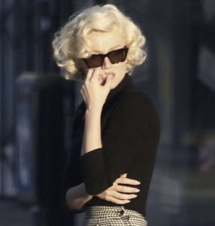 a woman with blonde hair and sunglasses is holding her hand to her face as she walks down the street