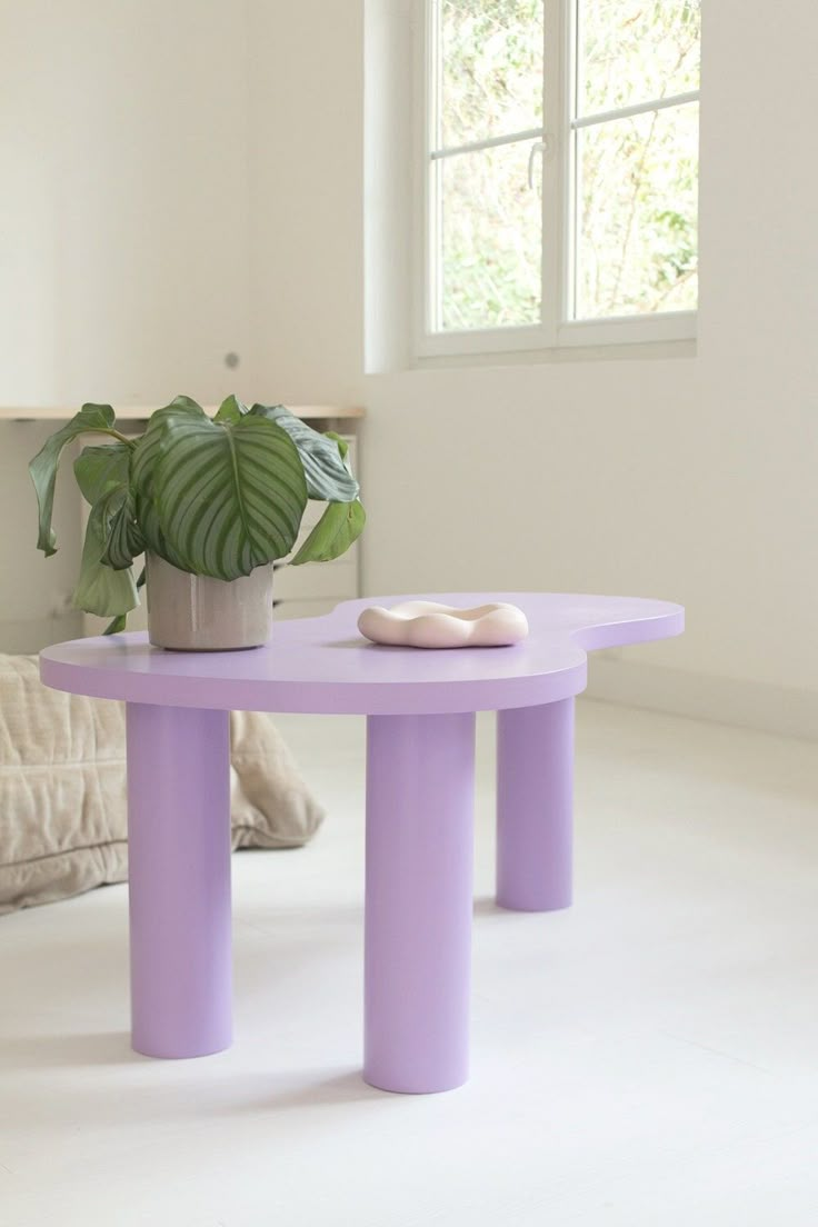 a purple table sitting in front of a window next to a potted green plant