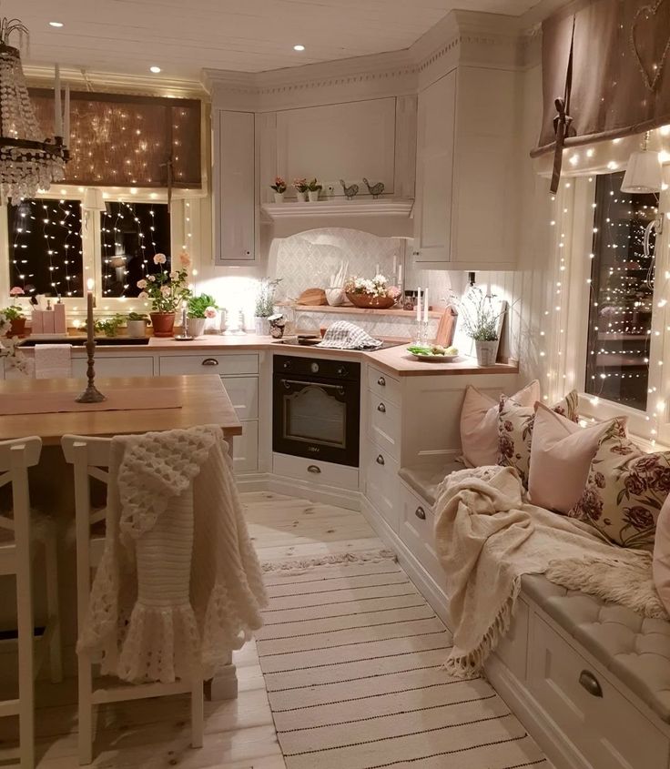 a kitchen filled with lots of white furniture and christmas lights on the windows sill