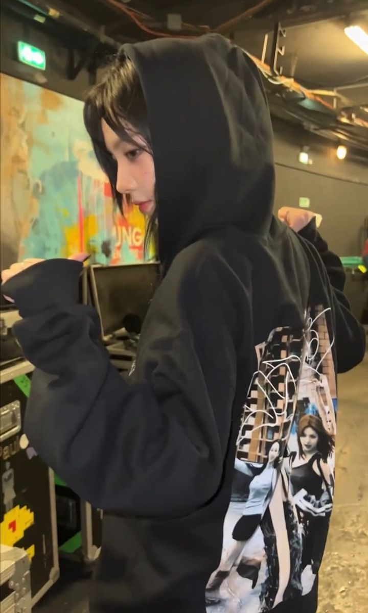 a young man wearing a black hoodie and looking at his cell phone in a parking garage