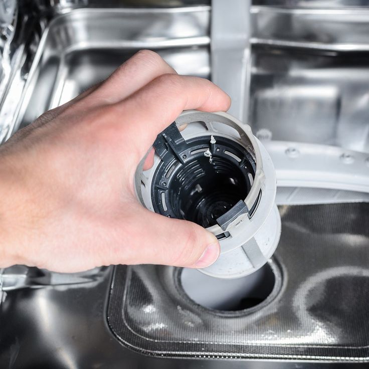 a hand is holding a camera lens in front of a metal sink with the lid open