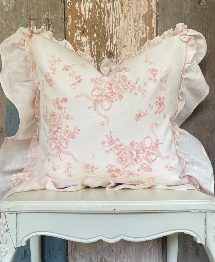 a pink pillow sitting on top of a white chair next to a wooden wall with peeling paint