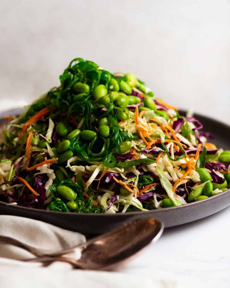 a salad with peas, carrots and sprouts in a black bowl on a white table