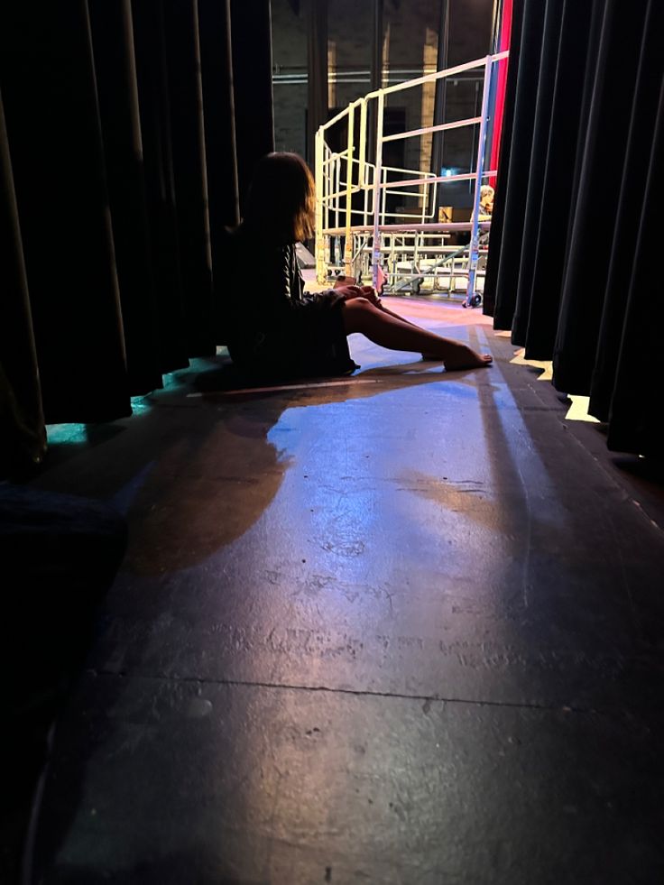 a woman sitting on the floor in front of a stage with black curtains and lights