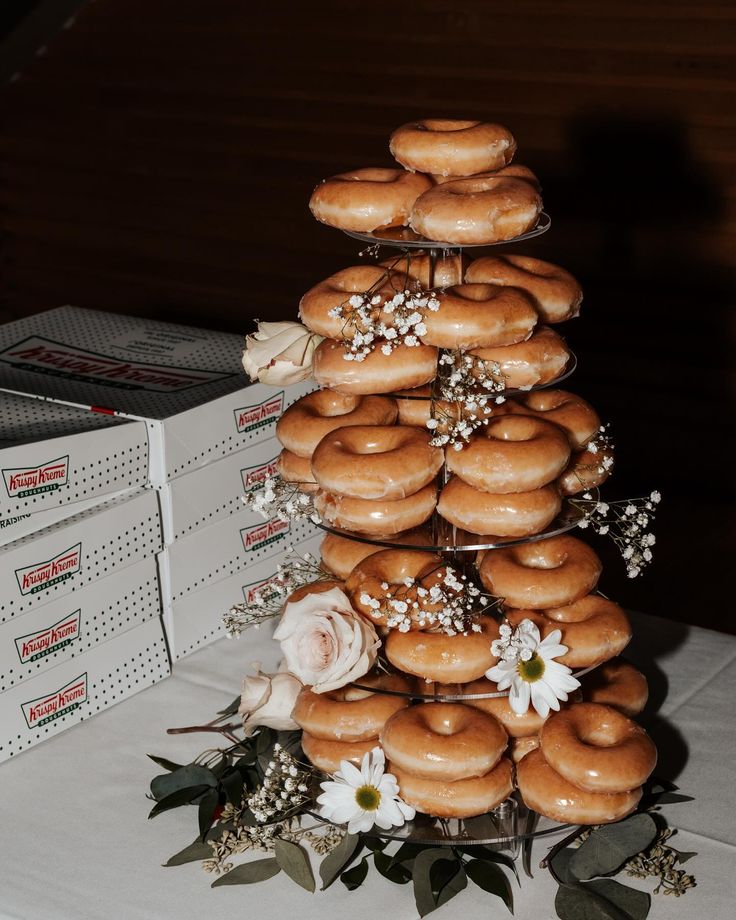 A Krispy Kreme donut tower with added wedding florals. Wedding Krispy Kreme, Donut Set Up Ideas, Krispy Kreme Donut Tower, Wedding Cake Donut Tower, Fun Wedding Dessert Ideas, Krispy Kreme Wedding Cake, Donut Tower Wedding, Krispy Kreme Donut Cake, Krispy Kreme Wedding