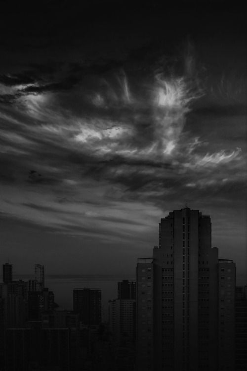 black and white photograph of city skyline with clouds in the sky at night, looking down on skyscrapers