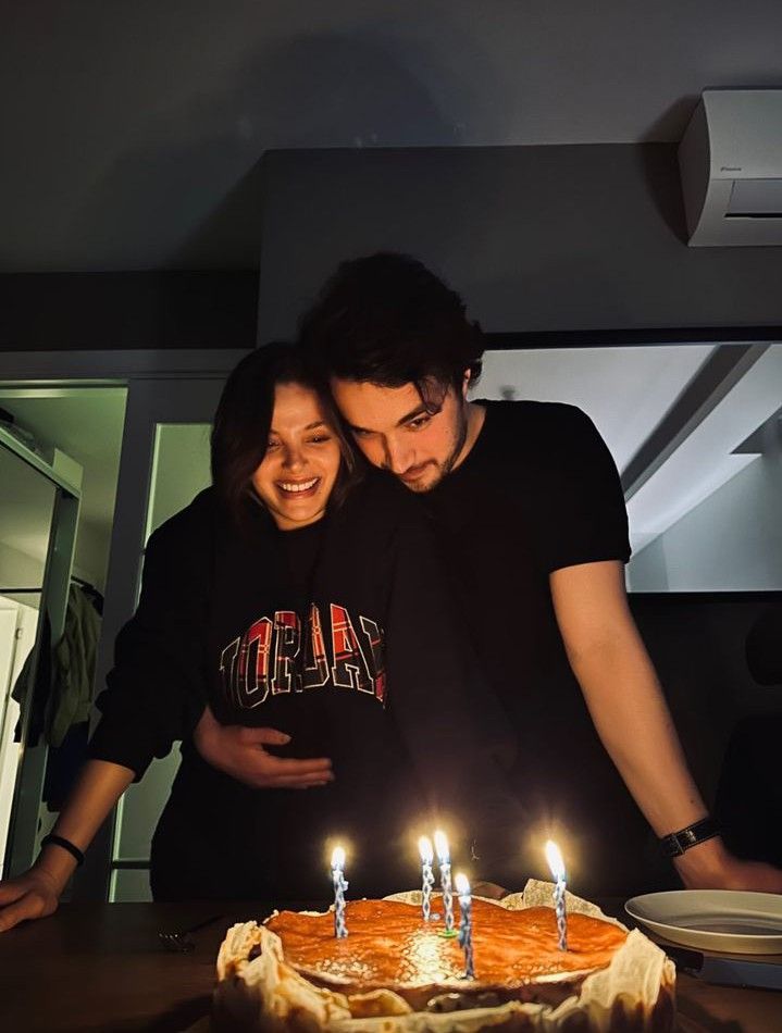 a man and woman standing in front of a cake with lit candles on it that says happy birthday