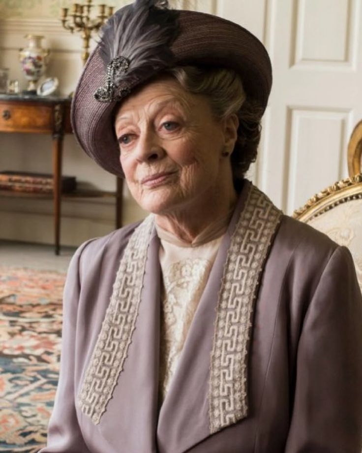 an older woman sitting in a chair wearing a hat and jacket with beading on it