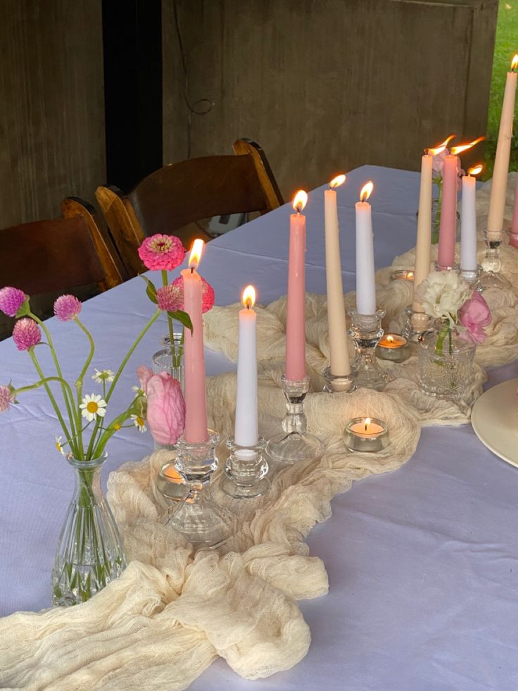 there are many candles on the table with pink flowers in vases and plates next to them