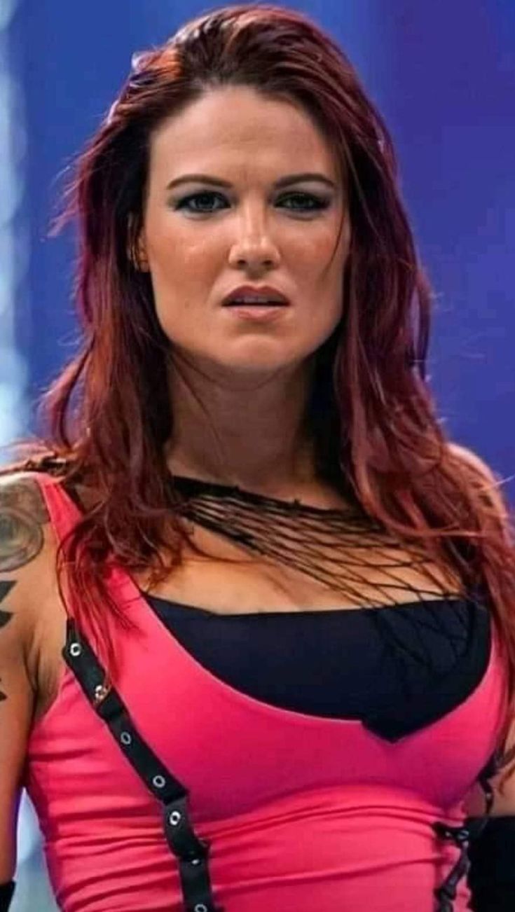 a woman with red hair and tattoos on her arm, wearing a pink top is looking at the camera