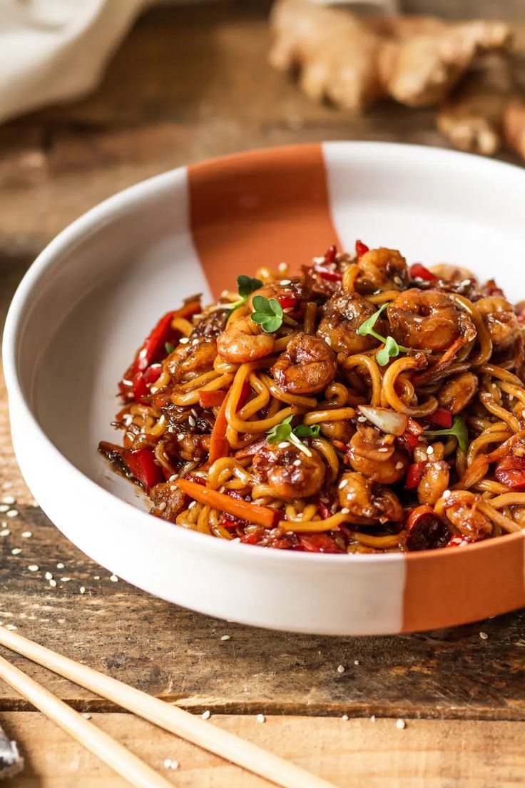 a white bowl filled with noodles and meat on top of a wooden table next to chopsticks