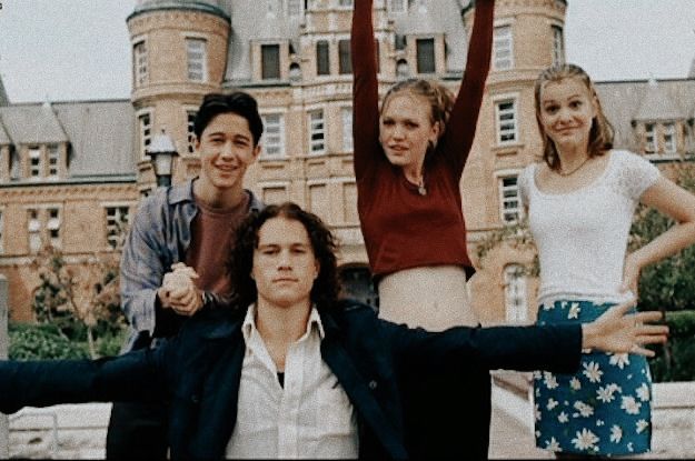 four people posing for a photo in front of a building with their arms raised up