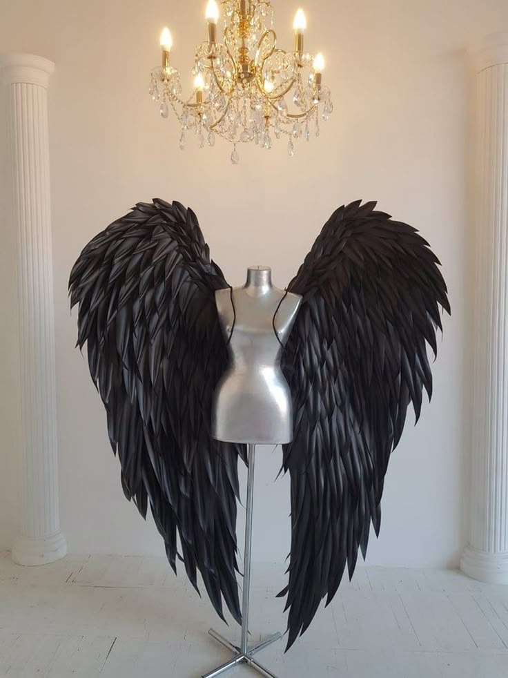 a mannequin with large black wings on it's head in front of a chandelier