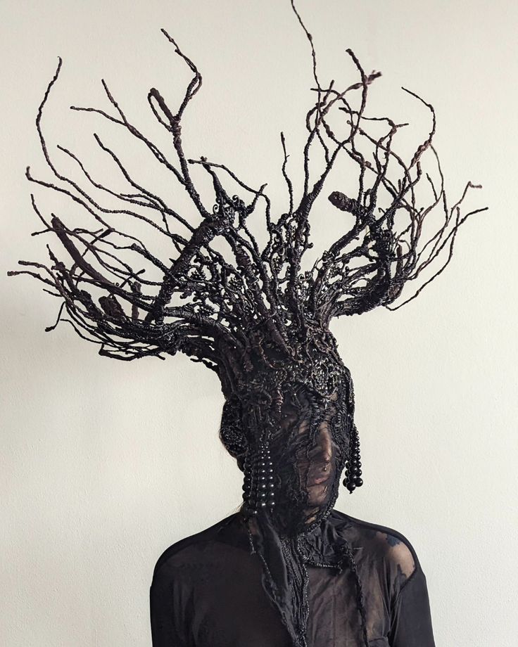 a woman with branches on her head is standing in front of a white wall and wearing a black shirt