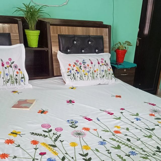 a bed with white sheets and colorful flowers on the bedspread, along with potted plants