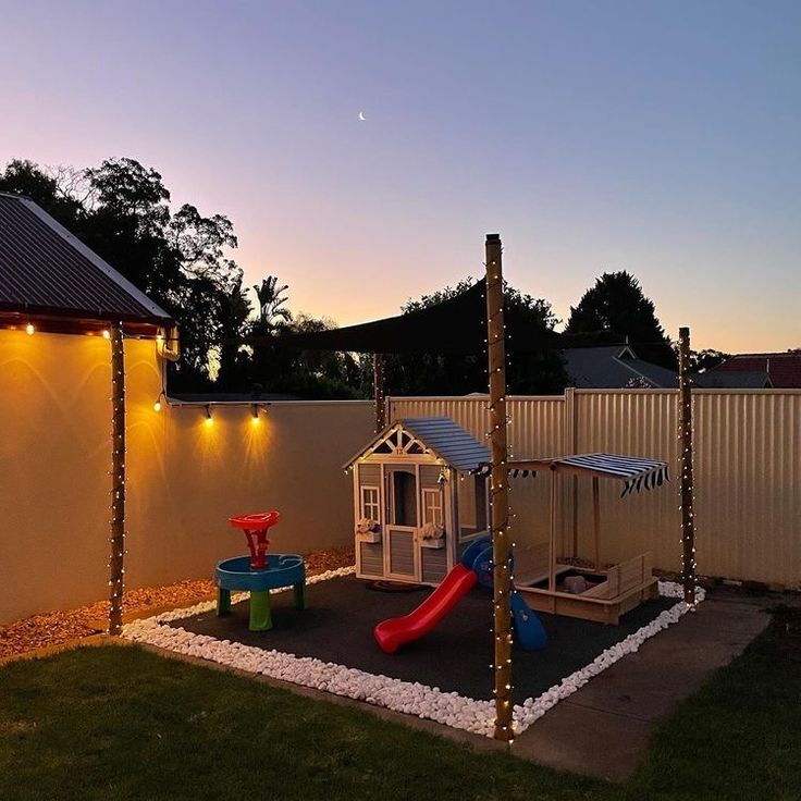 an outdoor play area is lit up at night with lights on the fence and in the back yard