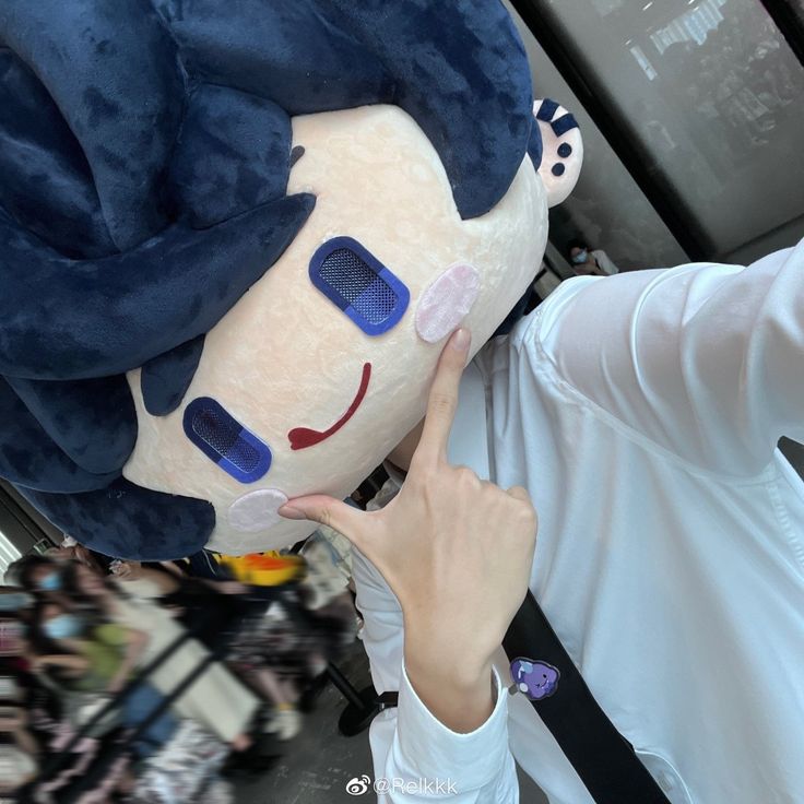 a person wearing a large blue and white stuffed animal with big eyes pointing to it's face