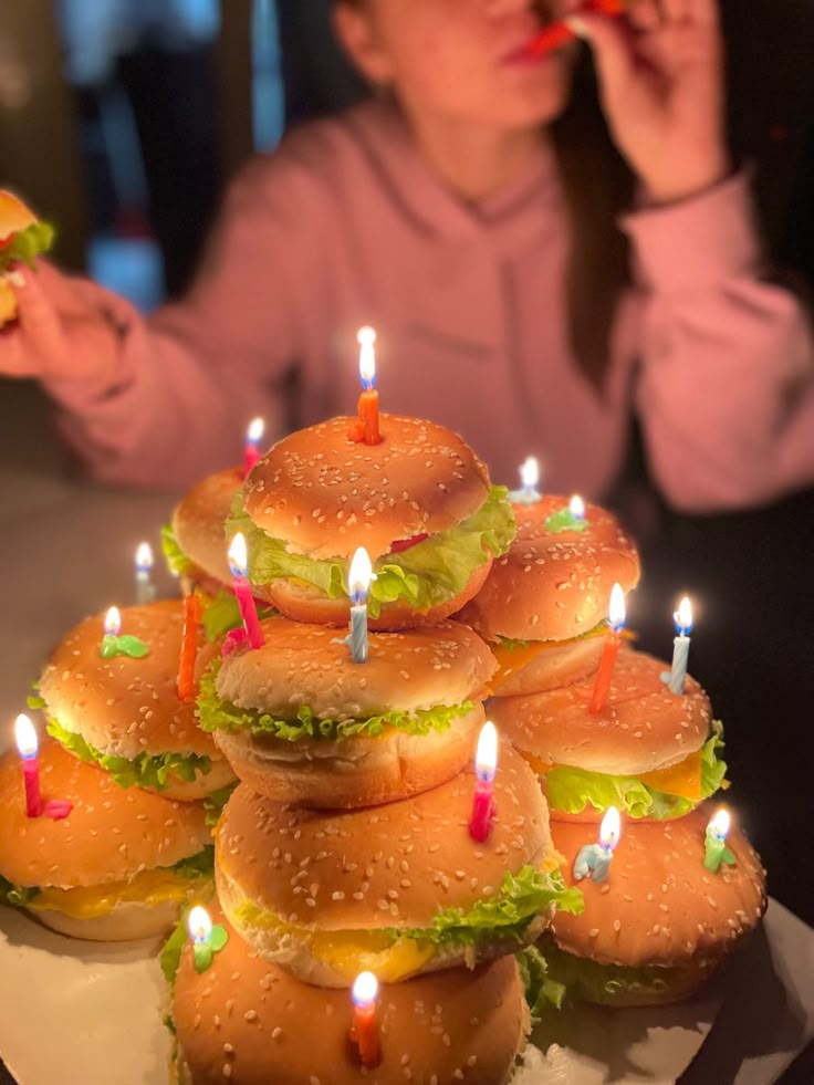 a woman is blowing out candles on hamburgers that have been stacked up with lettuce and tomatoes