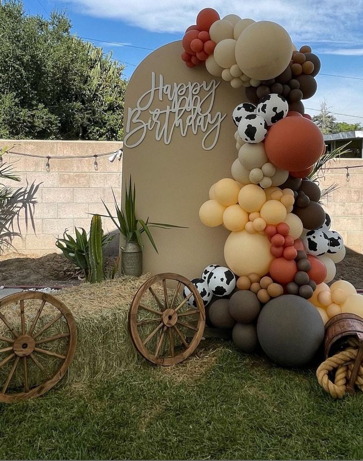 a birthday sign made out of balloons and other items on the grass in front of a horse - drawn wagon