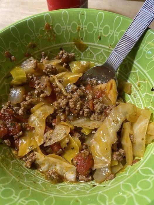 a green bowl filled with pasta and meat on top of a wooden table next to a red cup