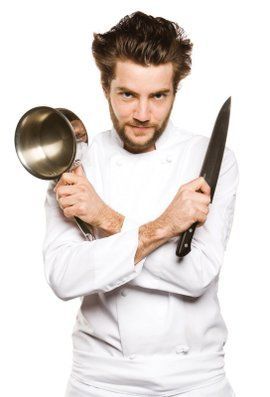 a man with a beard holding two large metal pans in one hand and a knife in the other