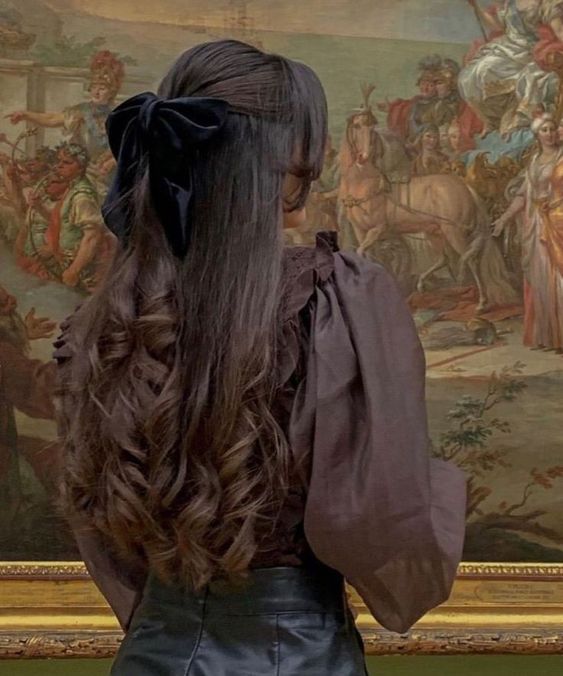 the back of a woman's head with long hair in front of a painting