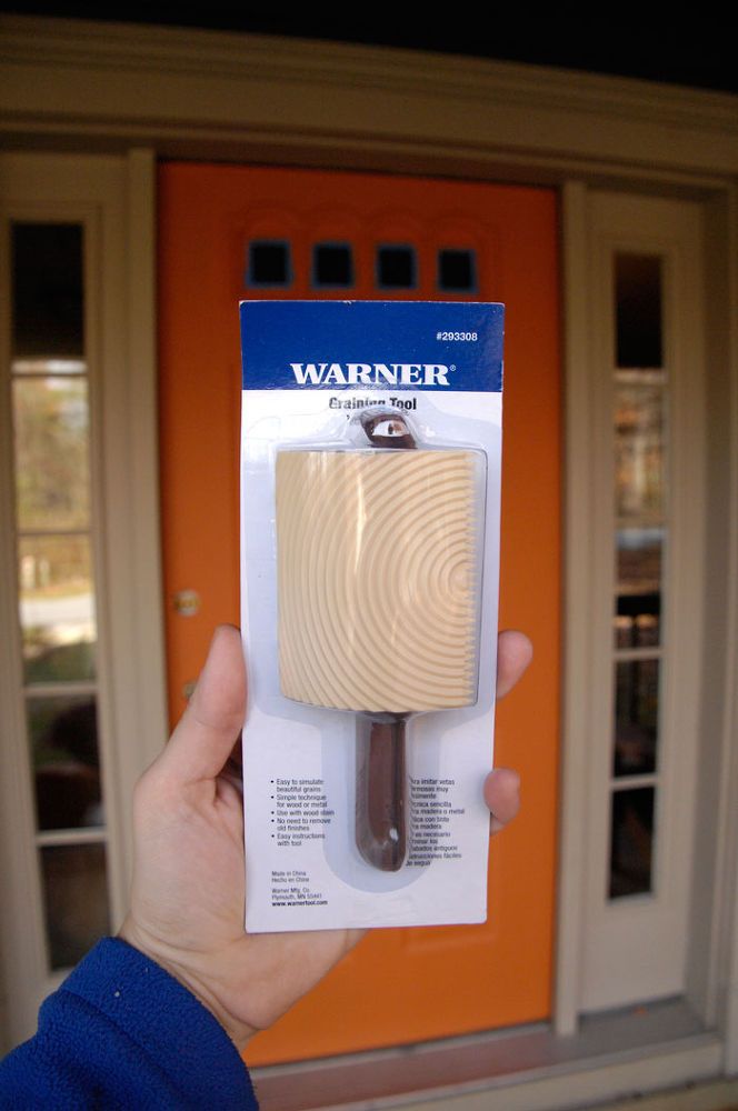 a person holding up a wooden object in front of a door with an orange background