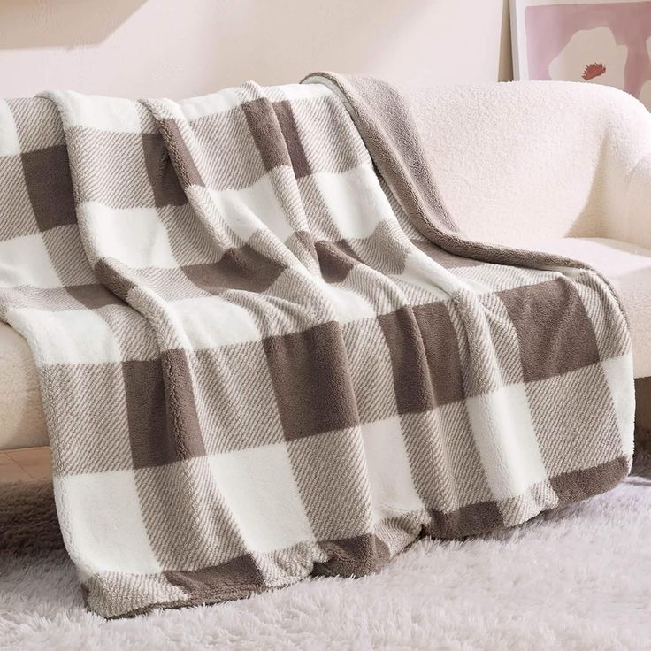 a white couch with a brown and white blanket on it's back next to a chair