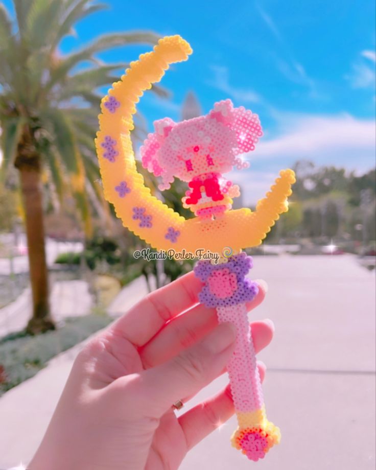 a person holding up a hello kitty keychain in front of a palm tree