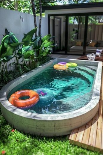 an inflatable pool surrounded by lush green plants and wooden decking, with lounge chairs around it