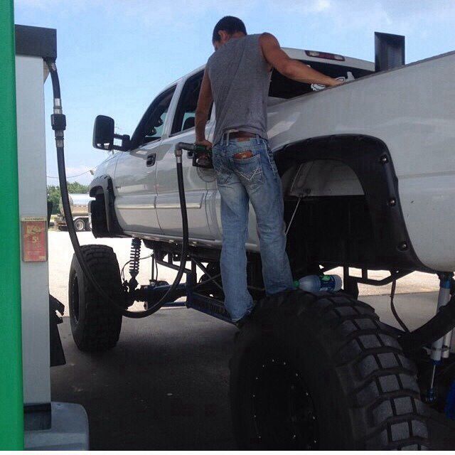 a man standing on the back of a white truck next to a gas pump and fuel can