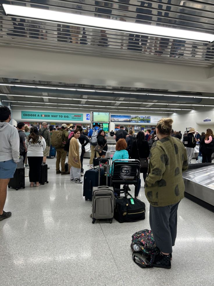 people waiting in line at an airport with their luggage and baggage carousels behind them