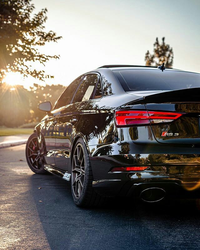 the back end of a black car parked in a parking lot with sun shining behind it