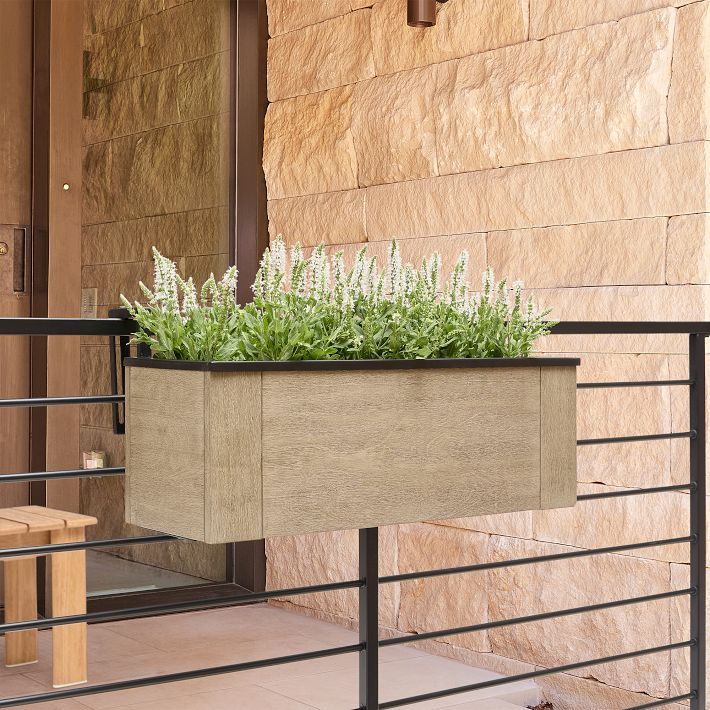 a planter with green plants in it sitting on a railing next to a building