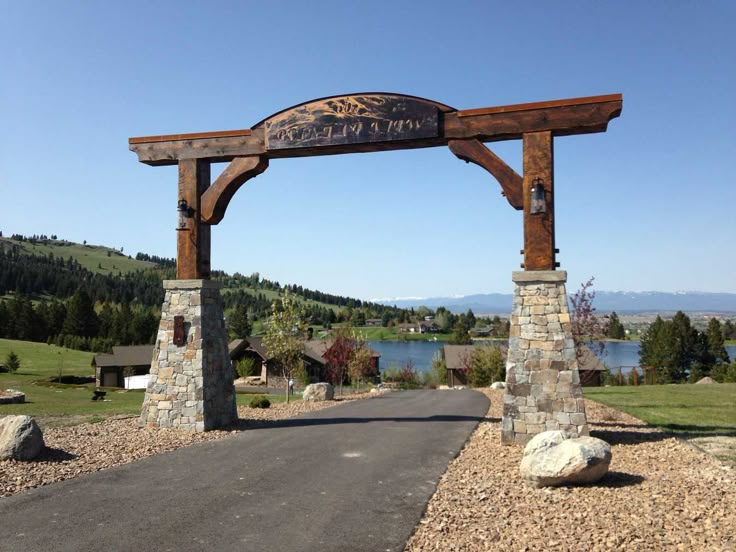 a wooden sign on the side of a road next to a body of water with mountains in the background