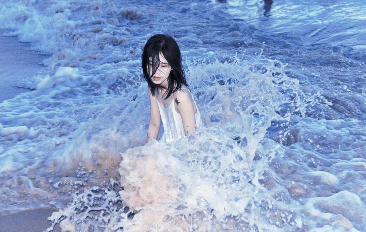 a woman is in the ocean with her hair blown up and water splashing around her