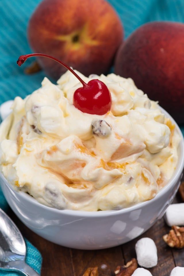 a bowl filled with fruit and whipped cream on top of a wooden table next to two peaches