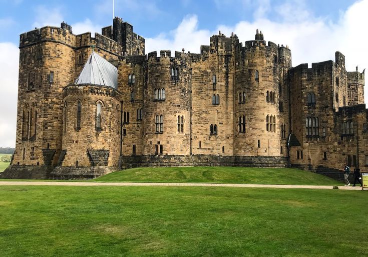 an old castle with grass in the foreground and people walking on the other side