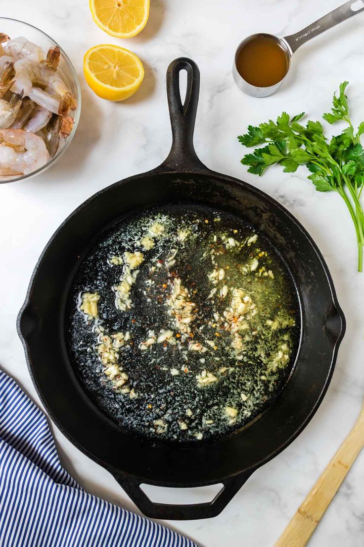 an iron skillet filled with food on top of a white counter next to lemons and parsley