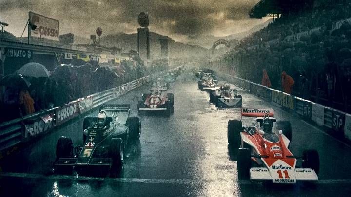 a group of racing cars driving down a wet track in front of a large crowd