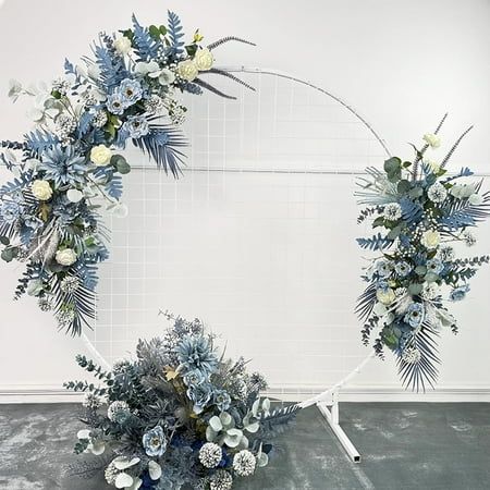 an arrangement of blue and white flowers arranged in a circle on a metal stand against a wall