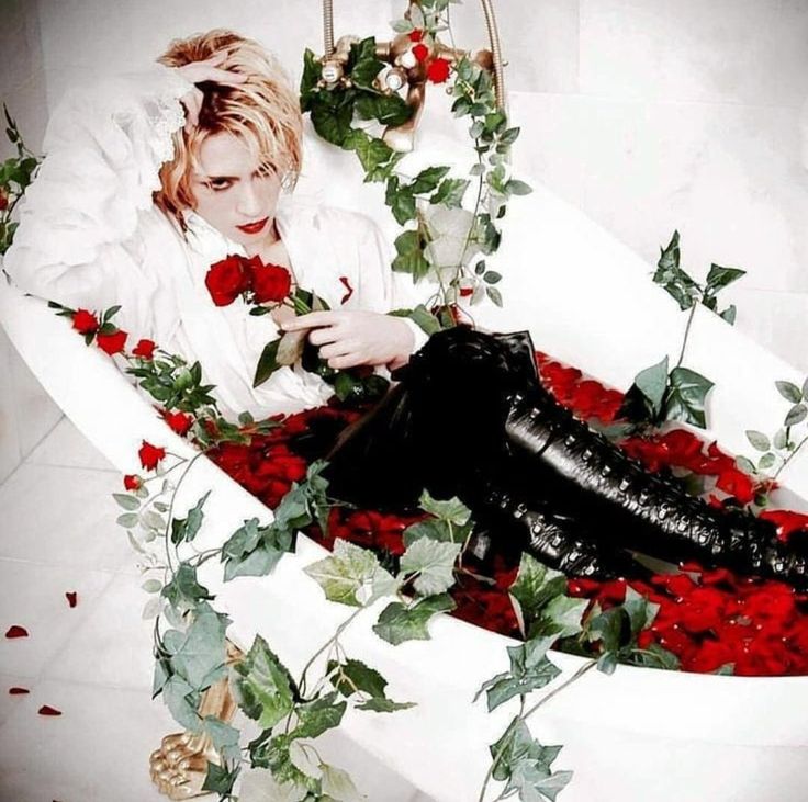 a woman sitting in a bathtub with roses on the floor and black leather boots