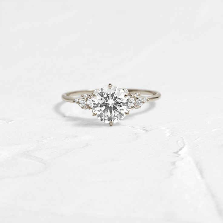 an engagement ring with three stones in the center on a white surface, close up