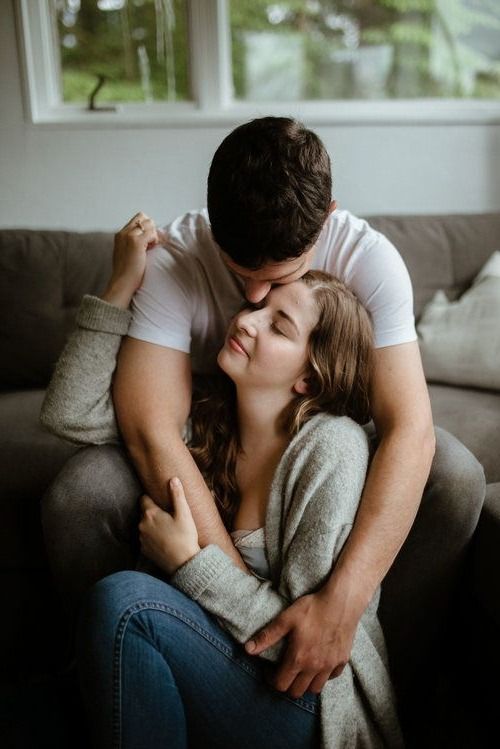 a man and woman sitting on top of a couch hugging each other in front of a window