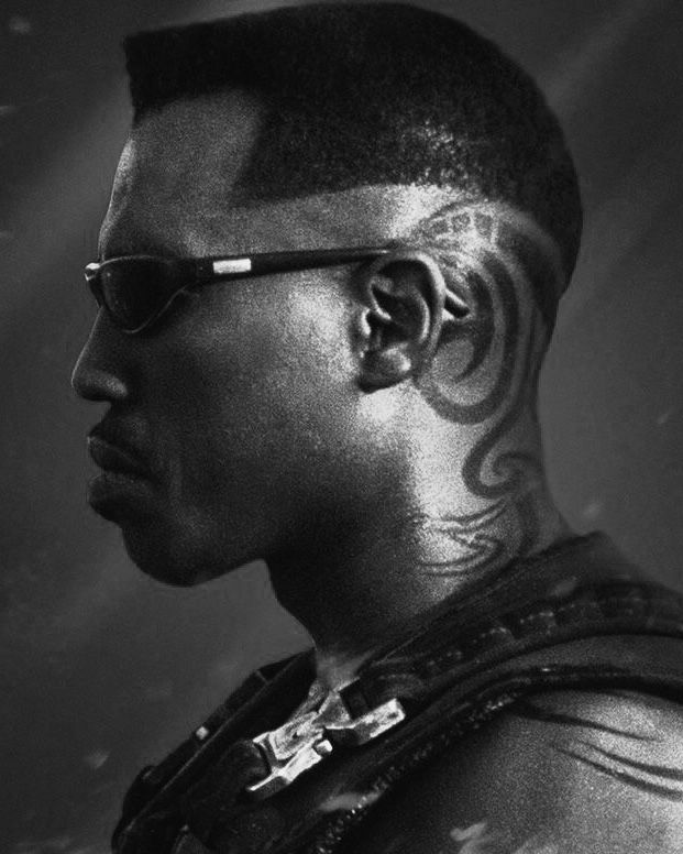 a man with tattoos on his face and neck, wearing sunglasses is looking off to the side